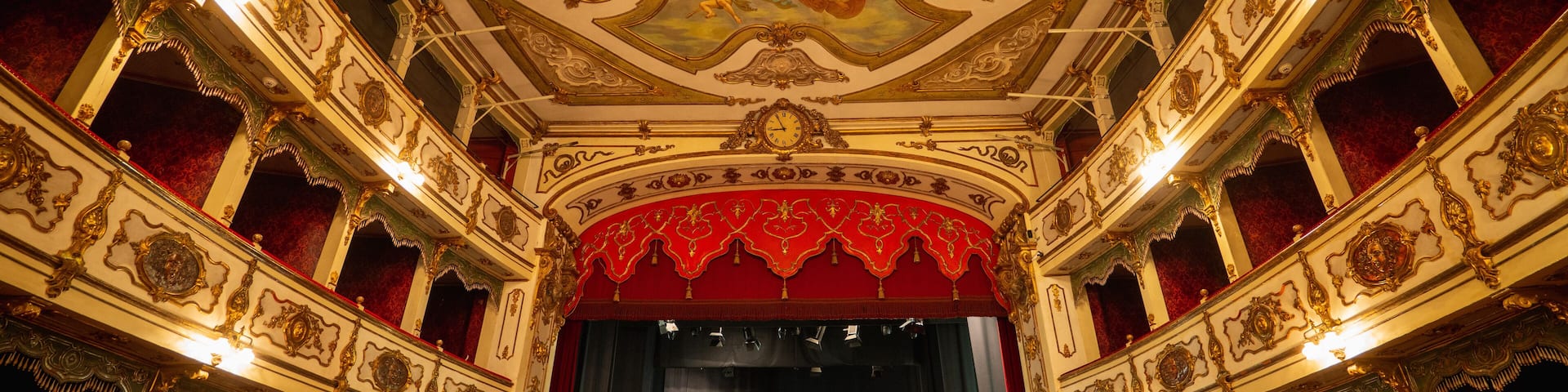 Wide shot of an Empty Elegant Classic Theatre with Big Stage and Red Velvet Curtains. Well-lit Opera House with Beautiful Mural Paintings Ready to Recieve Audience for a Play or Ballet Show
