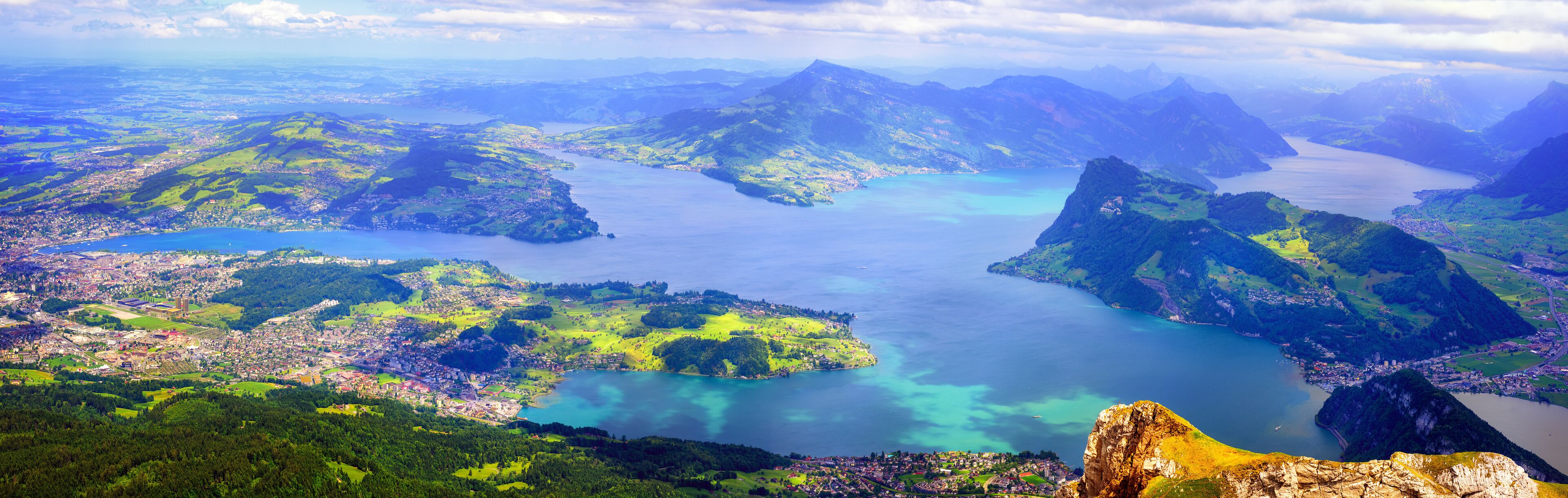 A mountainous landscape with a large lake surrounded by greenery and a town.
