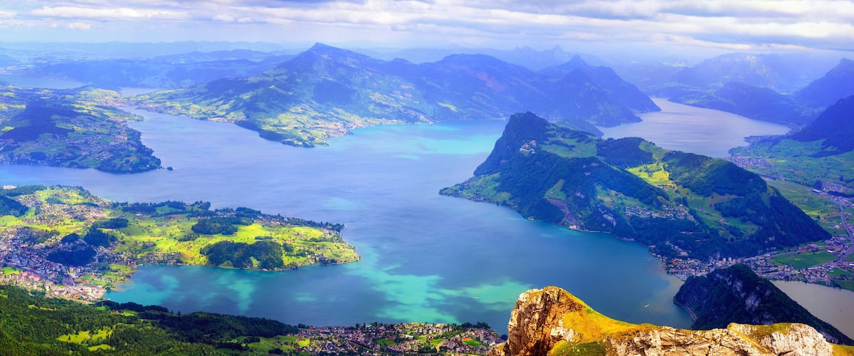 A mountainous landscape with a large lake surrounded by greenery and a town.