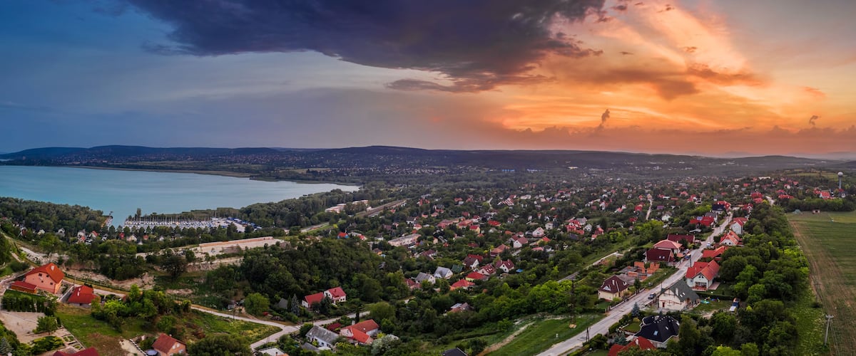 A coastal town with a mix of residential houses and open fields, a body of water, and distant hills.