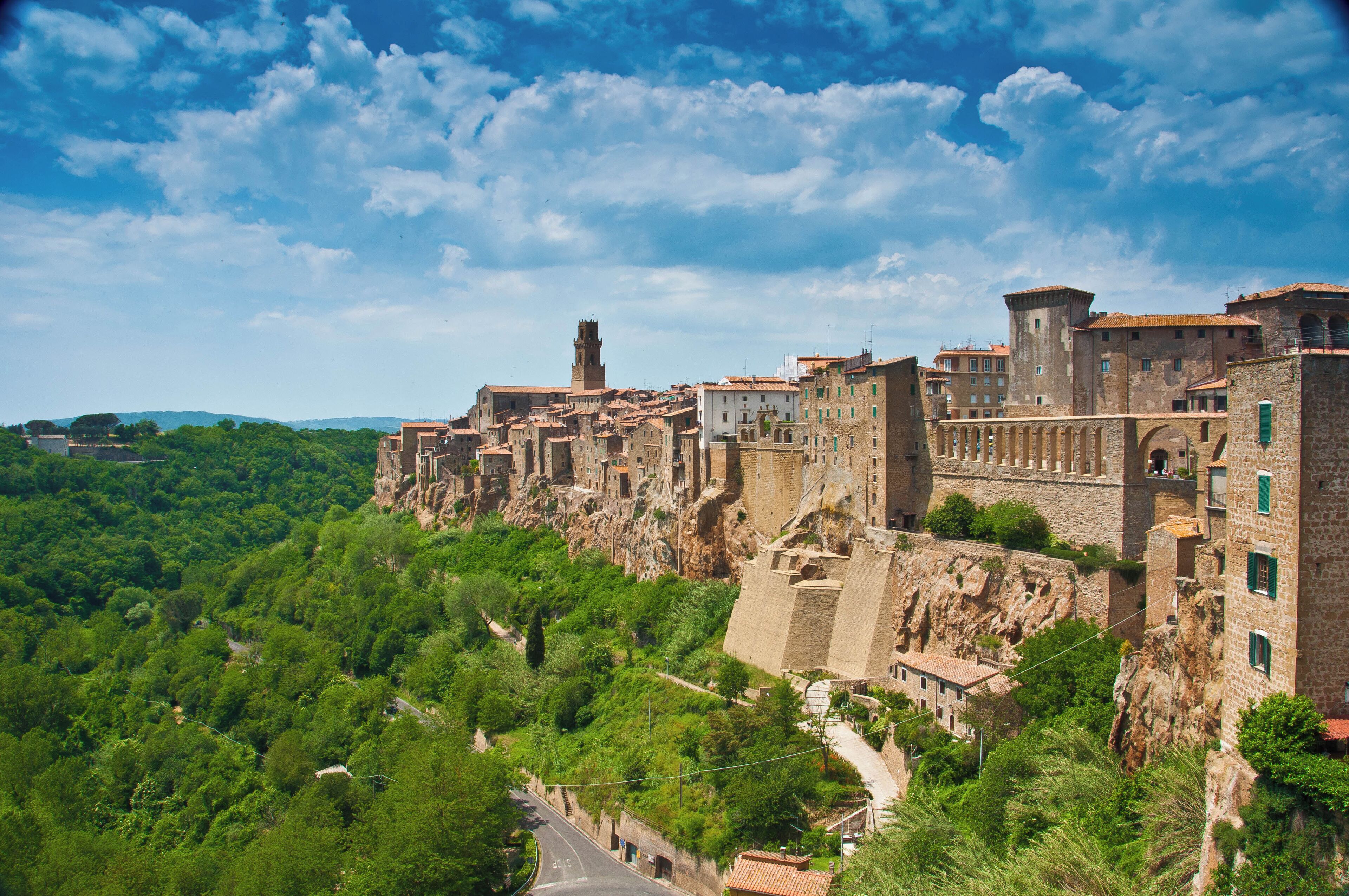 A historic town perched on a cliff with lush greenery, stone buildings, and a prominent tower.