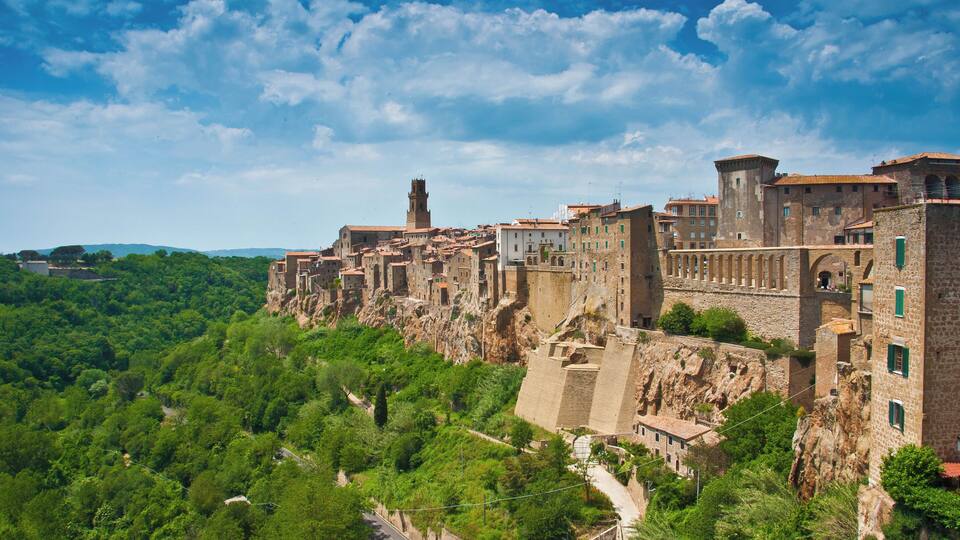 A historic town perched on a cliff with lush greenery, stone buildings, and a prominent tower.