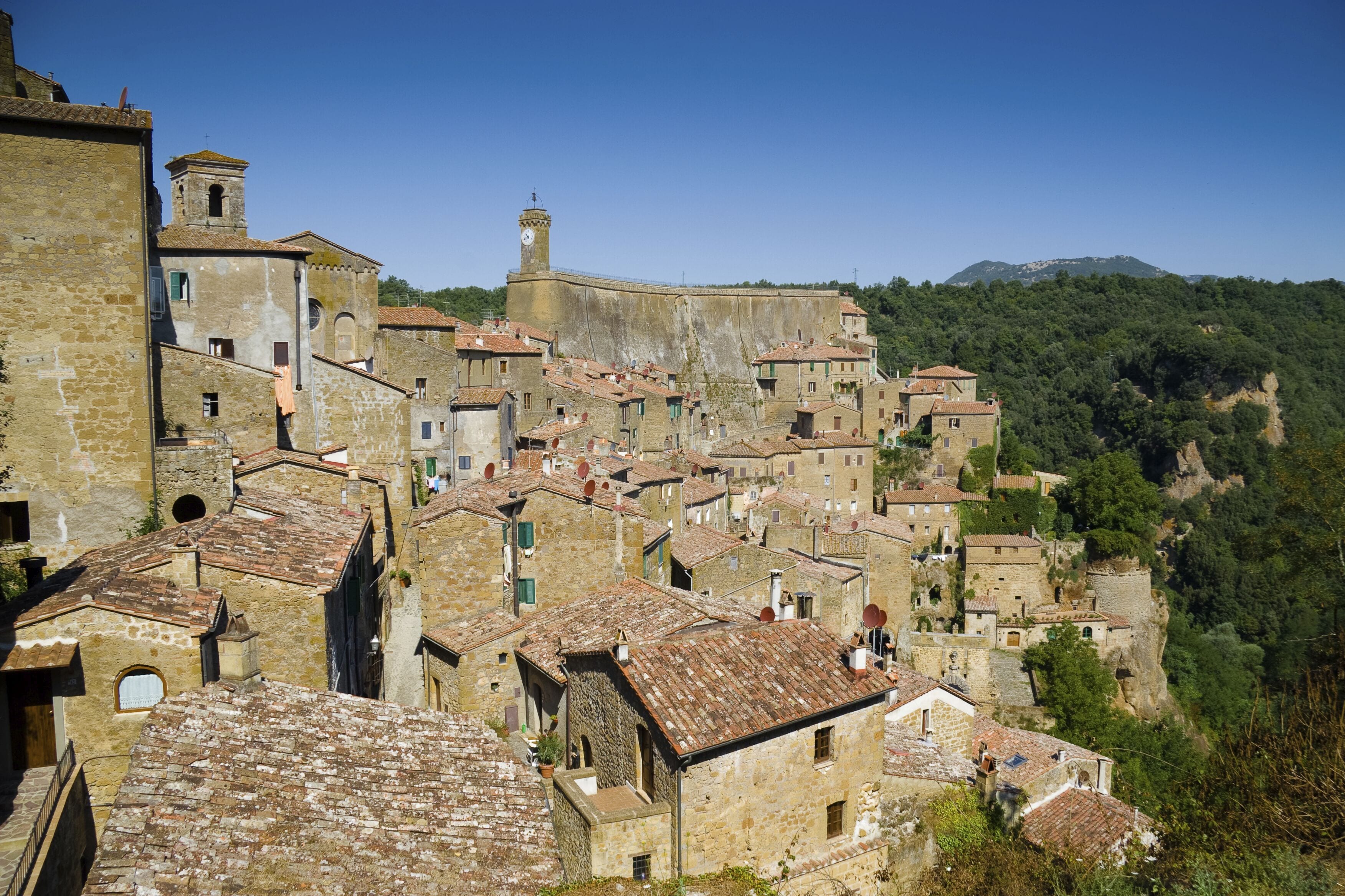 A historic town with stone buildings, a prominent church tower, and a hillside backdrop.