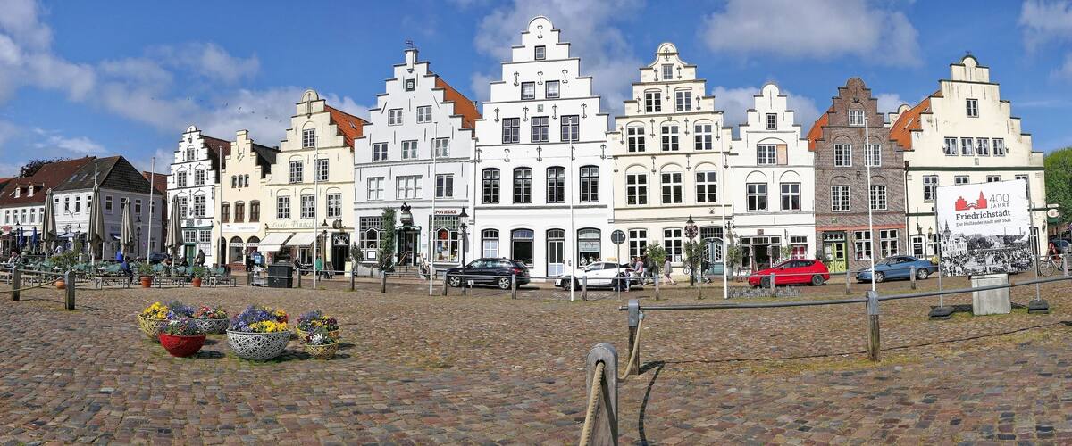 A cobblestone square with historic buildings, flower planters, and a sign indicating 400 years of Friedrichstadt.