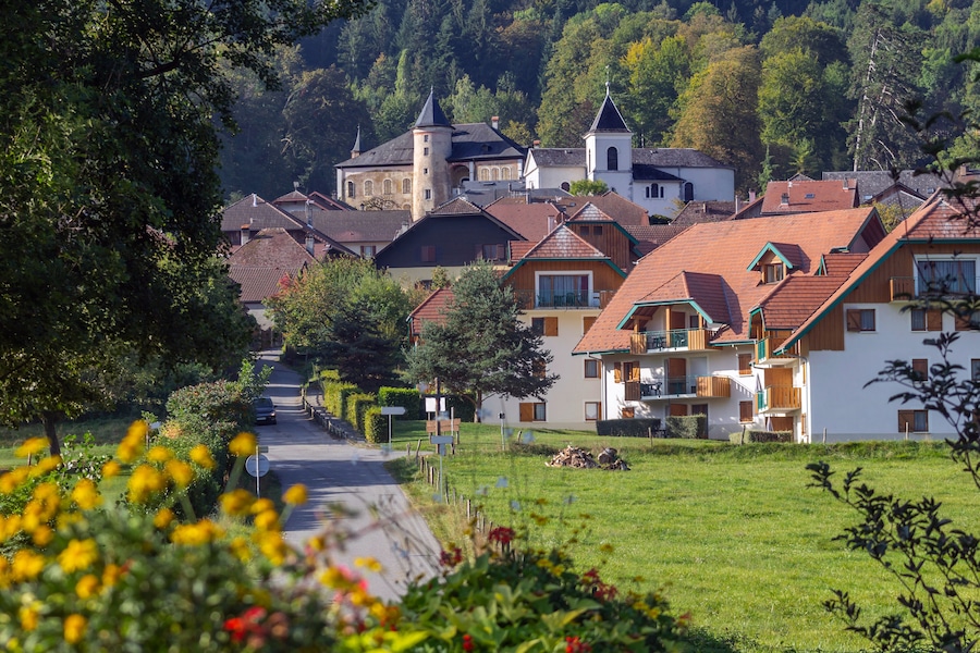Beautiful view of the Giez village: flowers in the foreground, the road and houses among the greenery and the castle on top, Savoy. Best villages of France