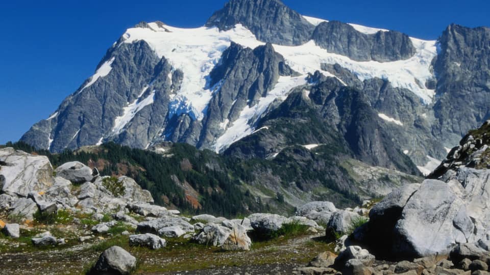 A mountain with a snow-capped peak and a clear reflection in a calm body of water.