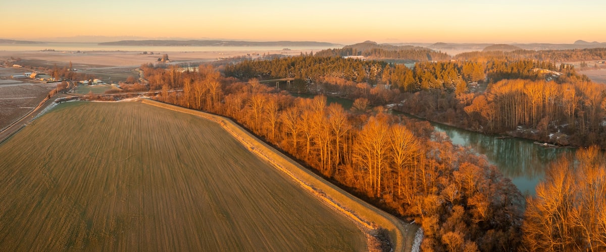 A river winding through a forested area with fields on either side.
