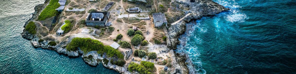 An aerial view of a rocky island with historical structures and clear blue waters.