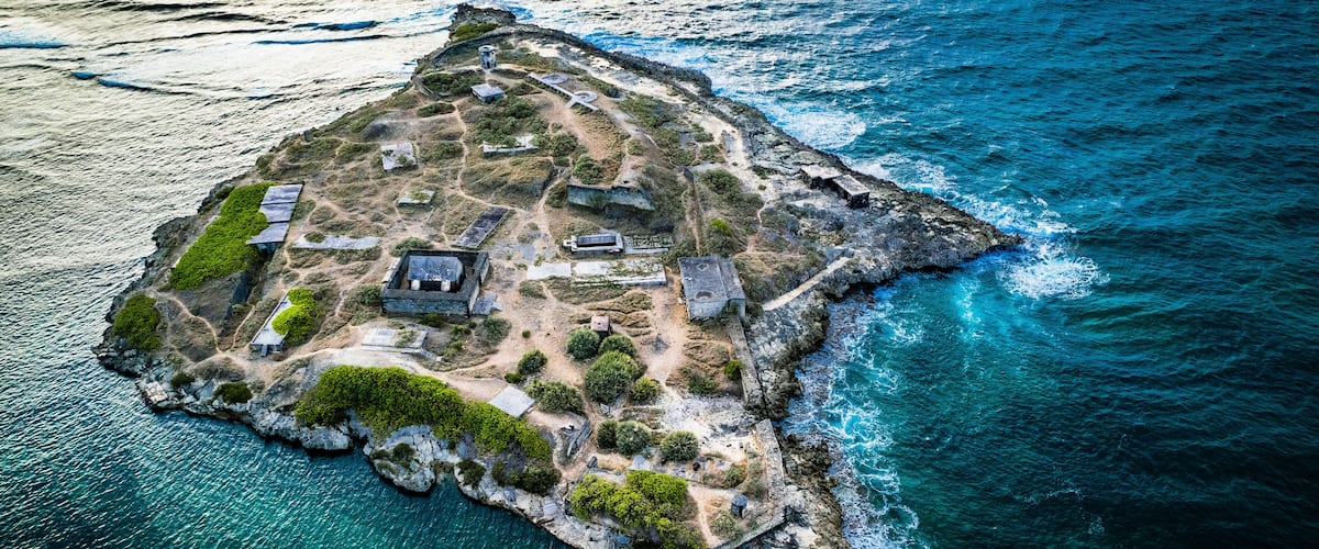 Vista aérea de una isla rocosa con estructuras históricas y aguas azul cristalino.