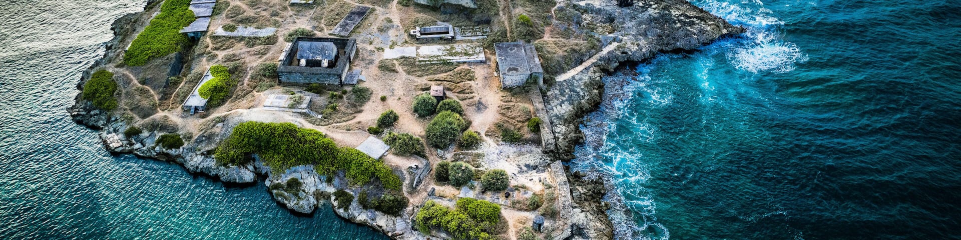 An aerial view of a rocky island with historical structures and clear blue waters.