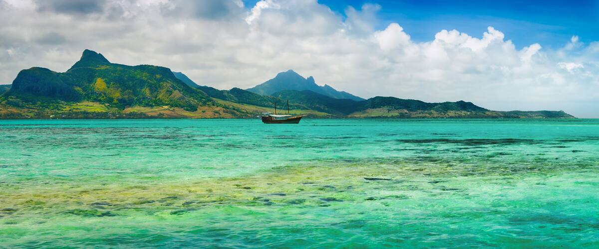 A boat on turquoise waters with a mountainous landscape in the background.