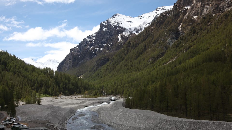 A river winding through a mountainous landscape with snow-capped peaks and dense forests.