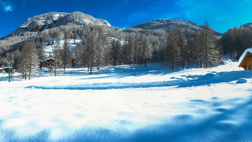 A snowy mountain landscape with a cabin and a person walking.