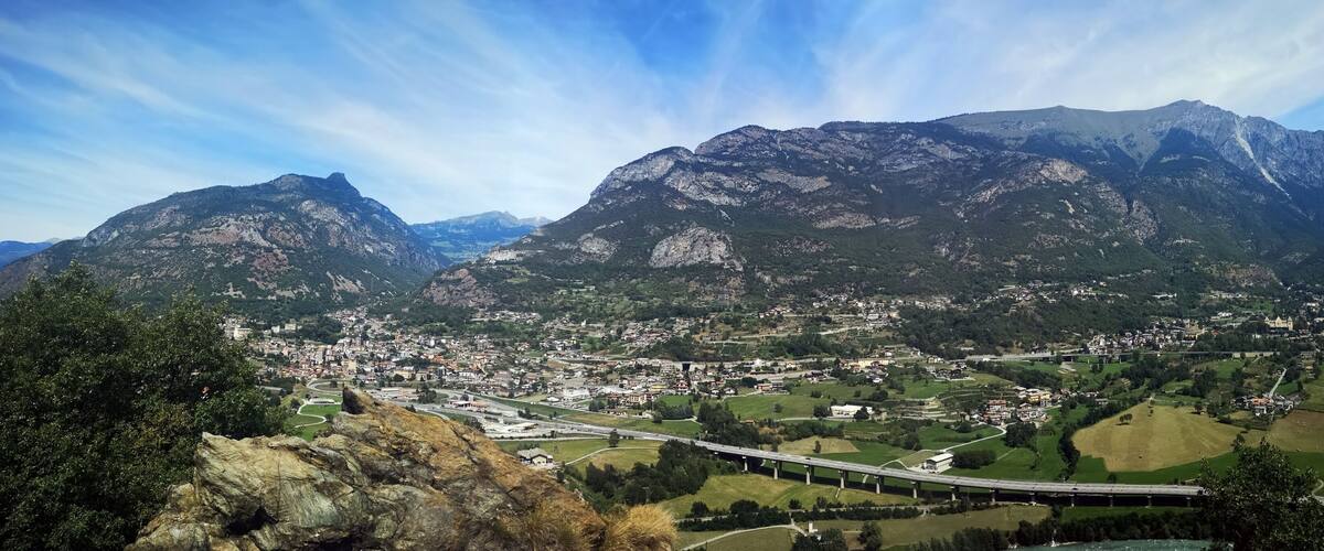 A mountainous landscape with a town nestled in the valley, a bridge crossing the valley, and a prominent mountain peak in the background.