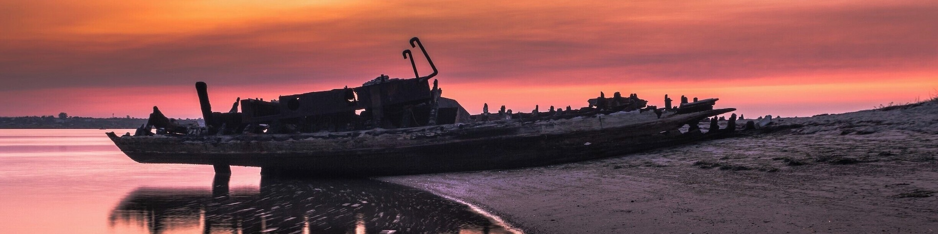 Ein Schiffswrack am Strand bei Sonnenuntergang.