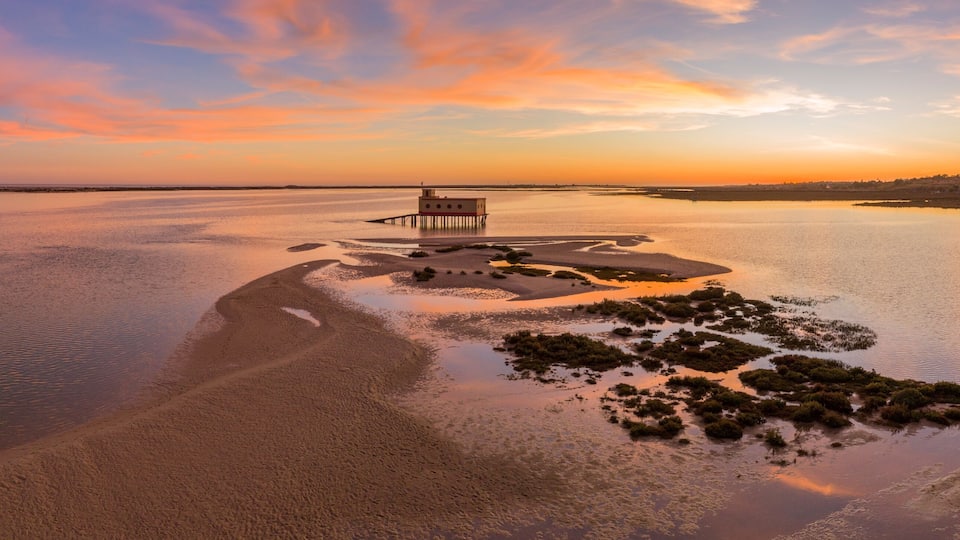 A sunset over a calm river with a pier and small islands.