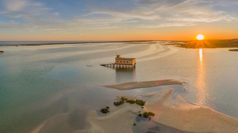 A coastal sunset with a pier and a small island with vegetation.