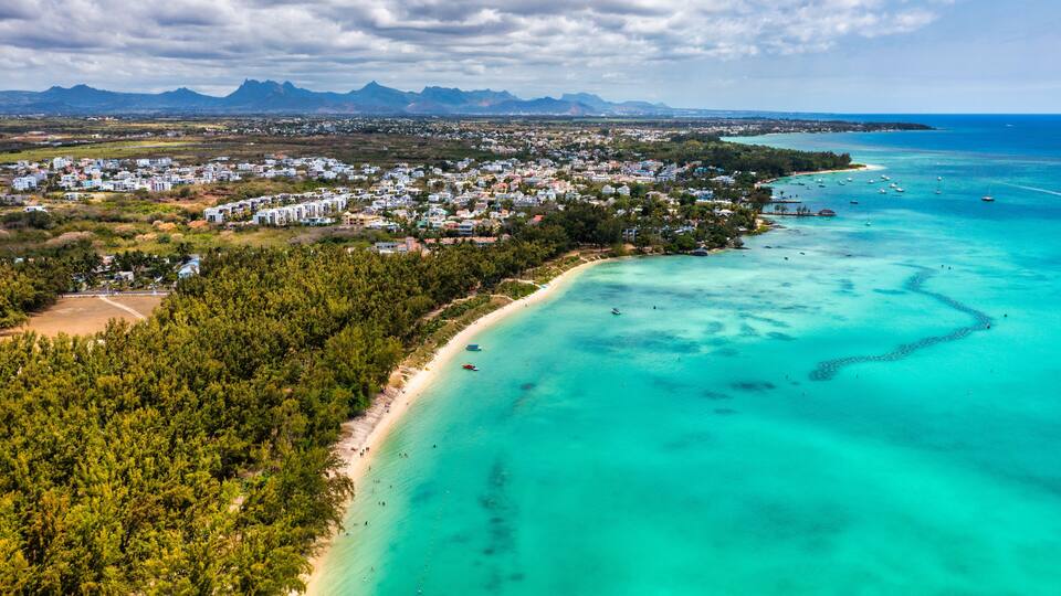 A coastal town with a beach, clear turquoise waters, and mountains in the background.