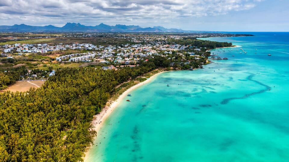 A coastal town with a beach, clear turquoise waters, and a mountainous backdrop.