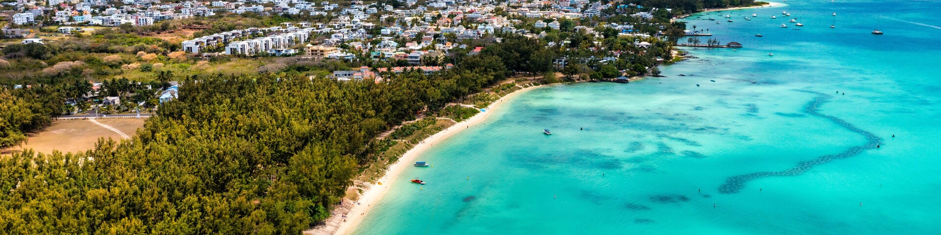 Un pueblo costero con playa, aguas turquesas cristalinas y montañas al fondo.