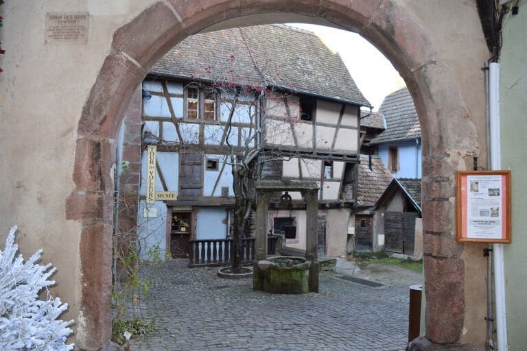 A medieval street with half-timbered houses, cobblestone pavement, and a stone archway.