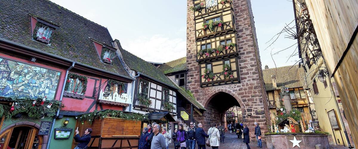 A historic town square with a prominent clock tower, traditional half-timbered buildings, and cobblestone streets.