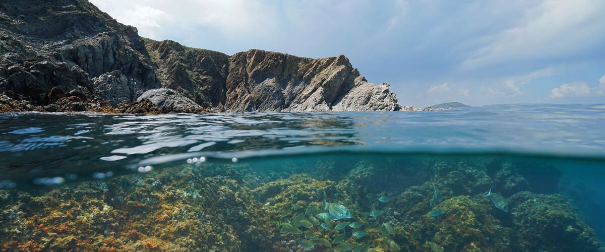 A coastal landscape with rocky cliffs and clear water revealing underwater coral reefs.