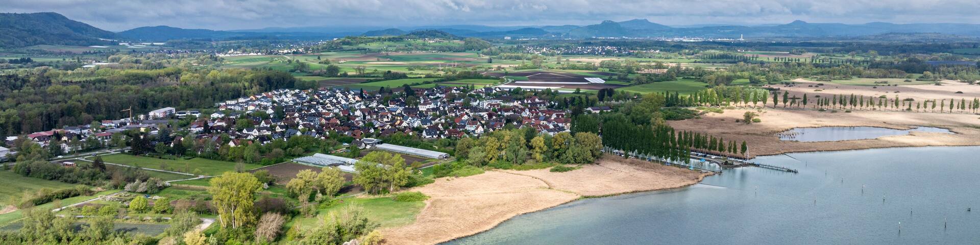 A lakeside town with a river, surrounded by greenery and distant mountains.