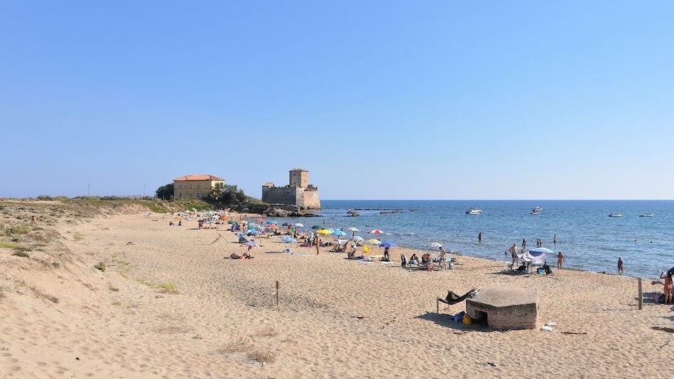 A sandy beach with people, umbrellas, and boats.