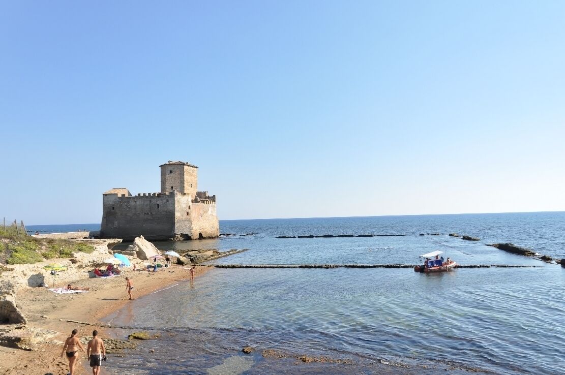 A coastal castle, a sandy beach, and a small boat in the water.