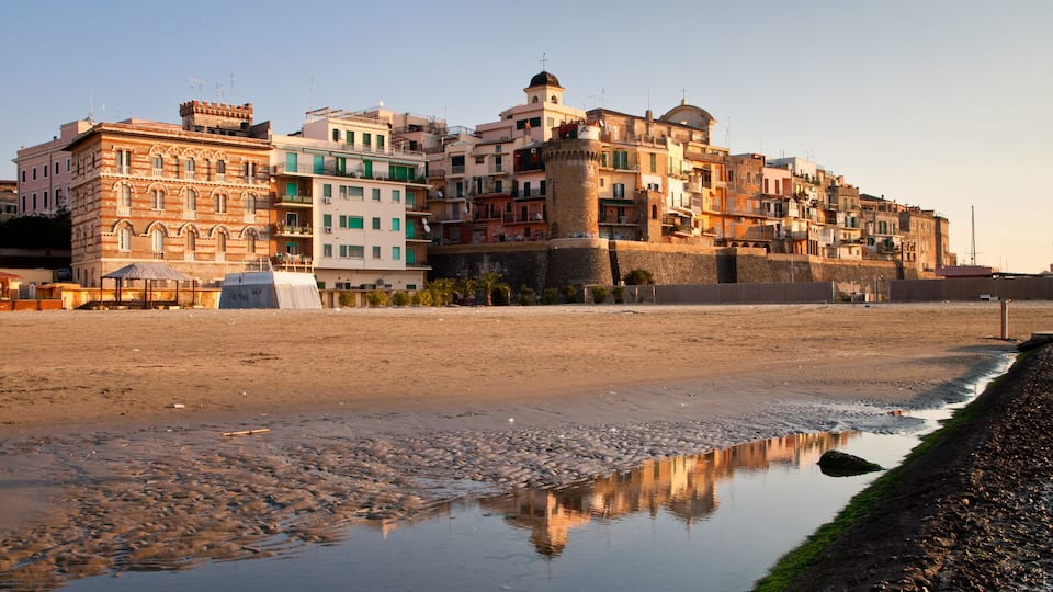 A coastal town with historic buildings, a prominent tower, and a reflective puddle on the beach.