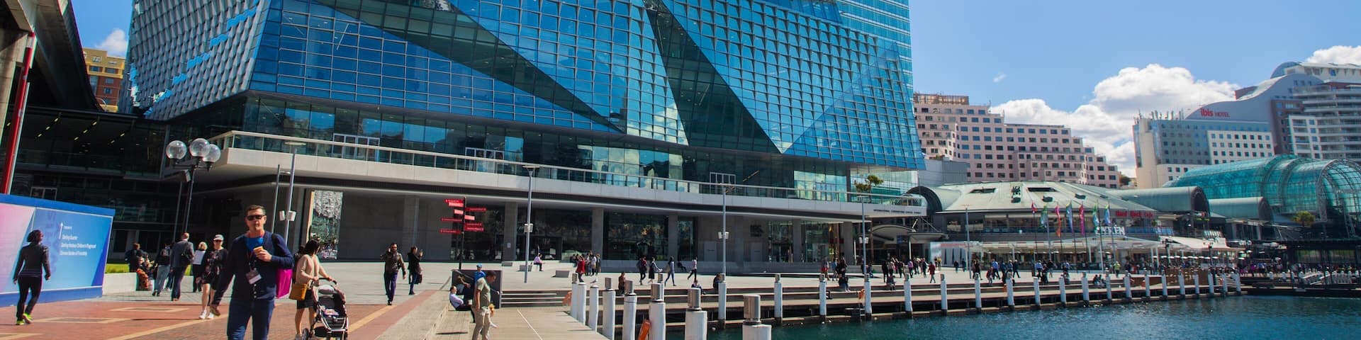 A modern building with a glass facade and a distinctive white roof, situated by a waterfront.