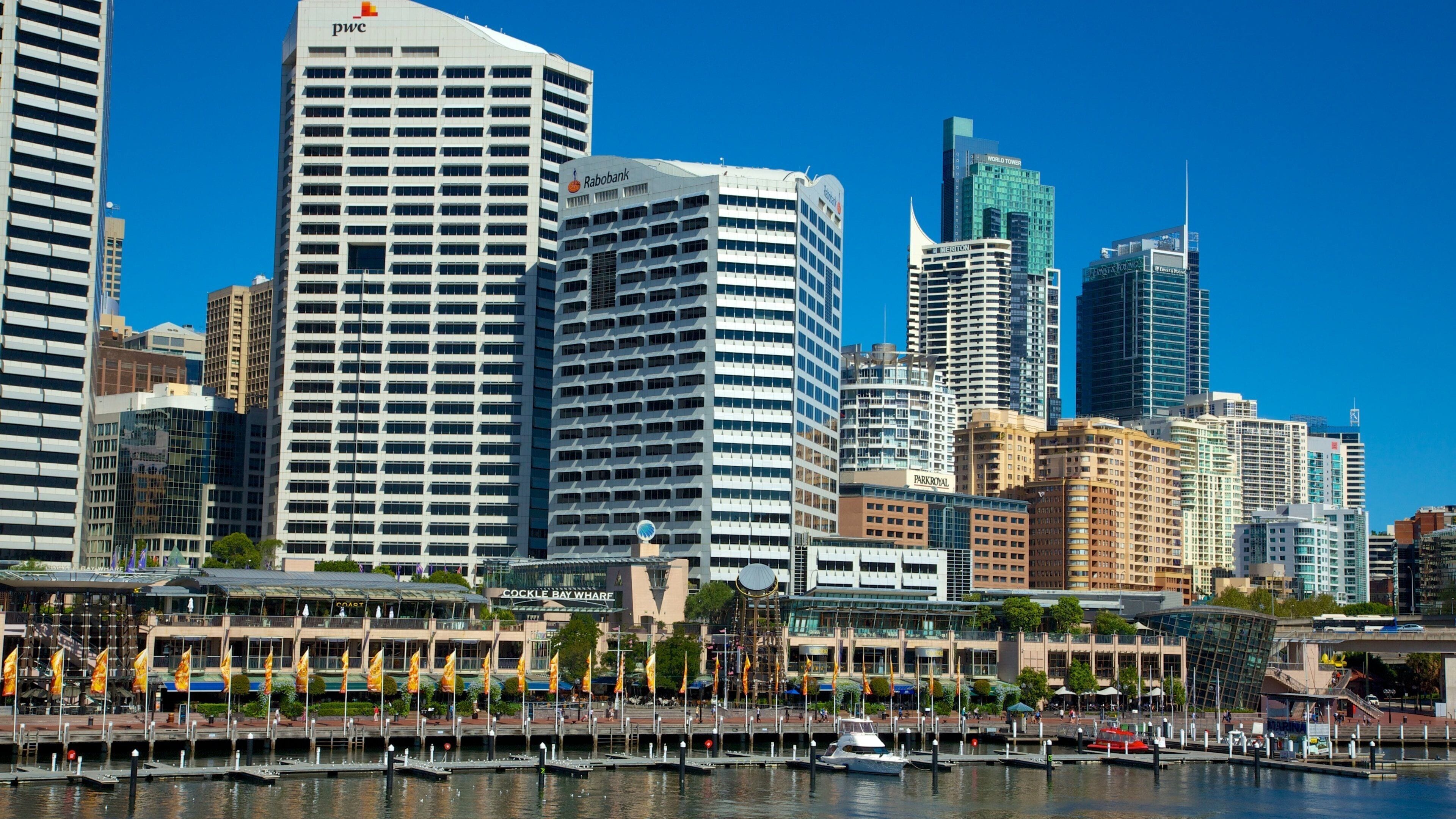A city skyline with modern skyscrapers, a marina with boats, and a waterfront promenade.