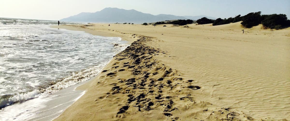 A beach with footprints leading to the water, a clear sky, and distant mountains.