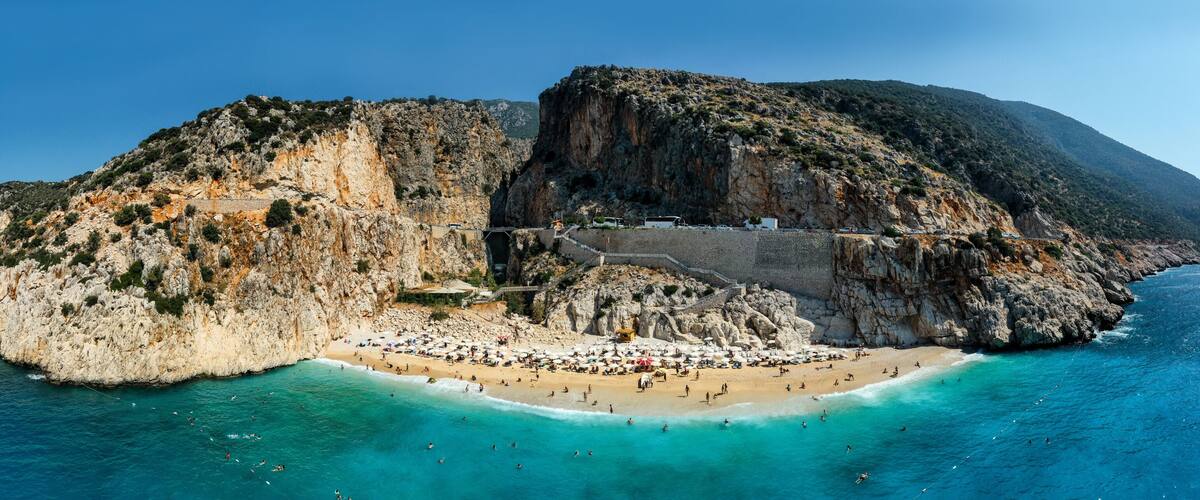 A coastal landscape with a rocky cliff, a beach, and a clear blue sea.