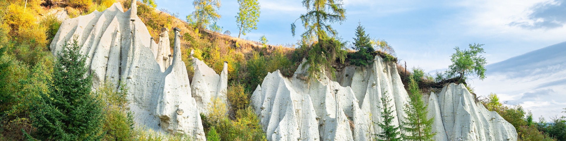 Un paisaje con formaciones rocosas blancas, árboles verdes y un cielo azul despejado.