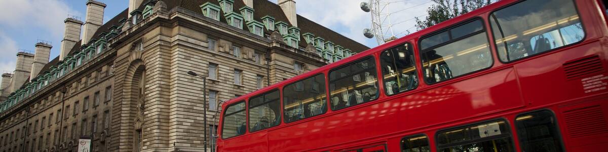 View of the iconic London Eye with a red double-decker bus in the foreground against a scenic backdrop of London architecture