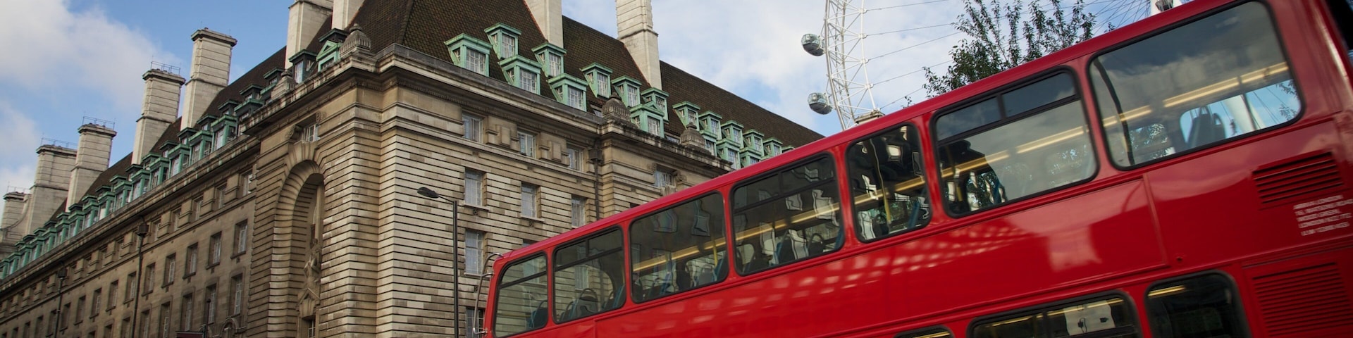 View of the iconic London Eye with a red double-decker bus in the foreground against a scenic backdrop of London architecture