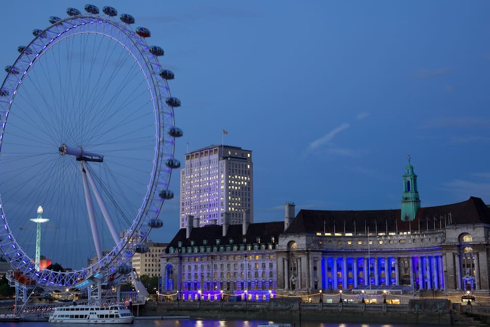 Una noria grande, un edificio histórico con iluminación azul y una torre verde.