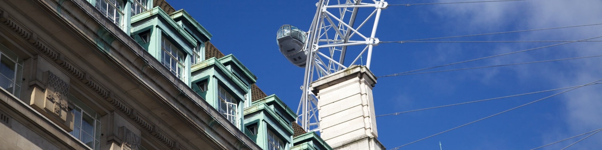 View of London Eye against a bright blue sky with historic architecture in the foreground