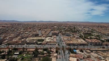 A sprawling cityscape with dense urban development, a prominent central road, and distant mountains.