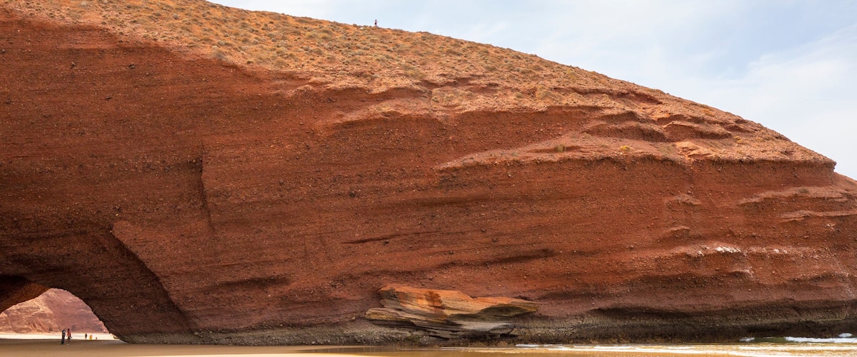 A large red rock formation with a natural archway.