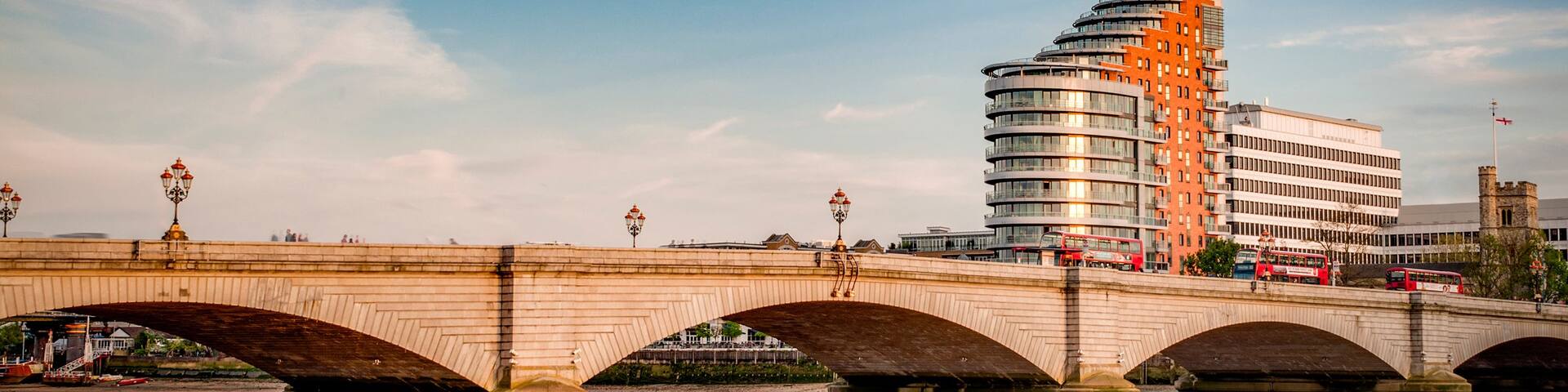 A stone bridge over a river with modern buildings in the background.