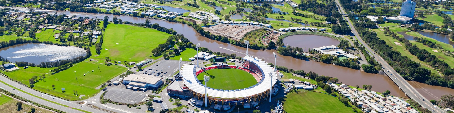 An aerial view of a stadium surrounded by green fields, a river, and a highway.