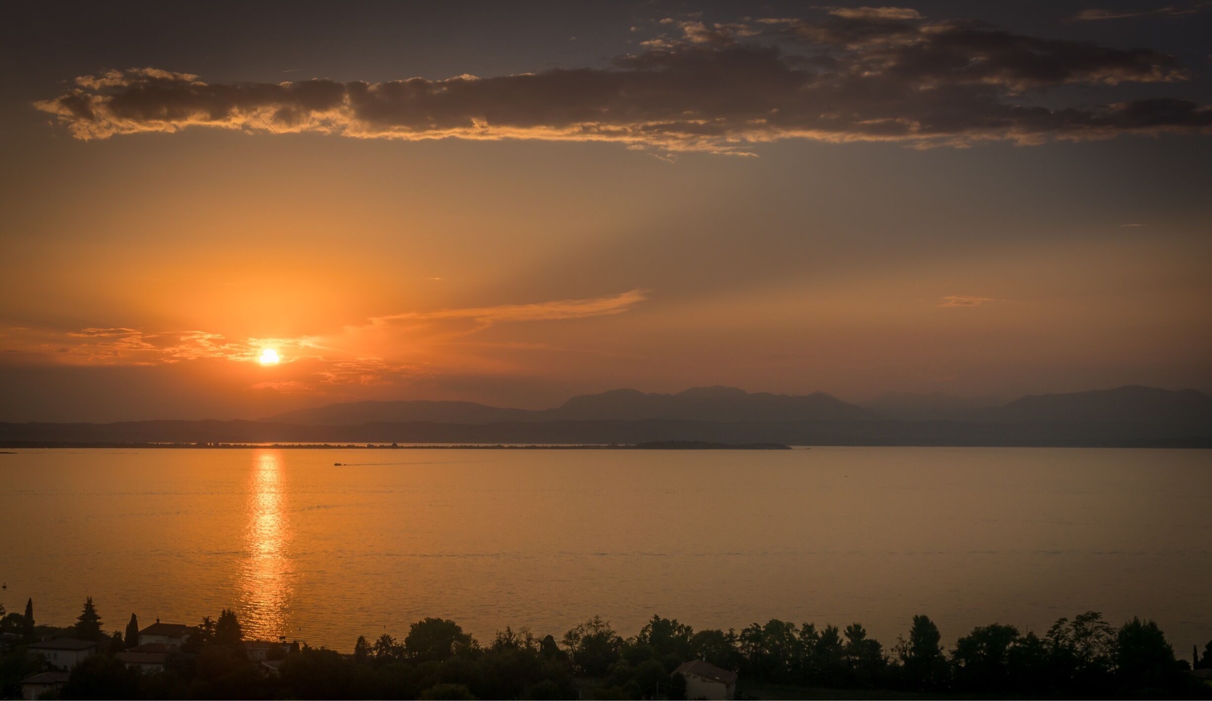 A sunset over a calm body of water with distant mountains and a silhouette of a town.
