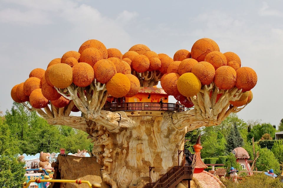 A tree with orange spherical decorations and a small house on its branches.