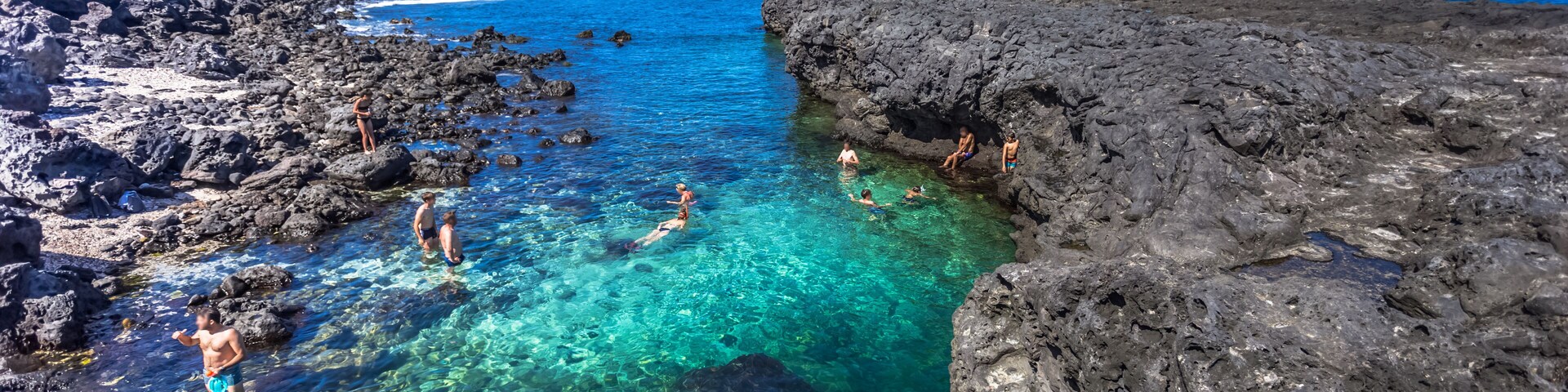 Mar azul transparente con costas rocosas y gente nadando.