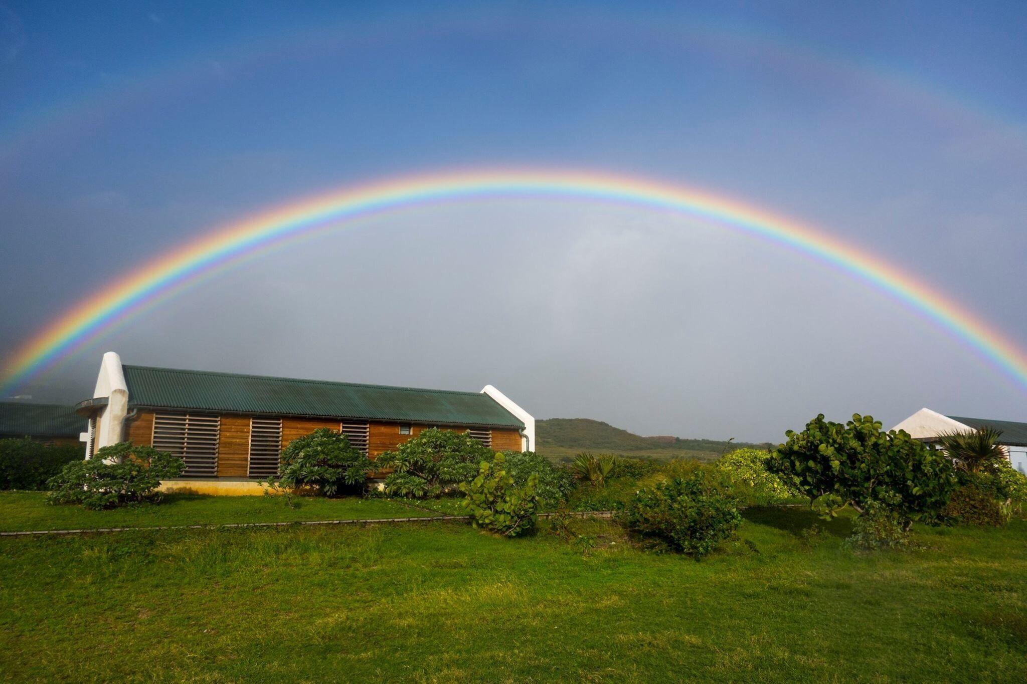 A house with a green roof and a rainbow in the background.