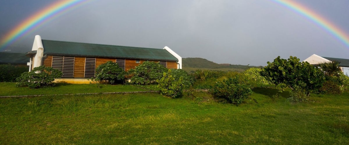 A house with a green roof and a rainbow in the background.