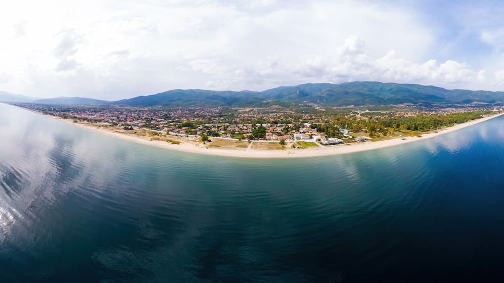 Une vue aérienne d’une ville côtière avec une plage, des montagnes en arrière-plan et des eaux calmes.